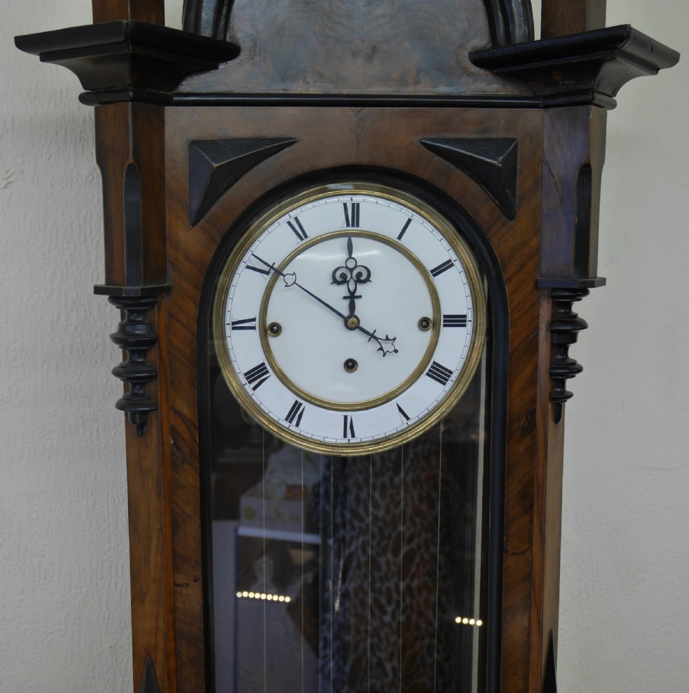 A 19th-century walnut Vienna regulator wall clock featuring a glazed front door, three brass weights, and a white enamel dial with Roman numerals. View III