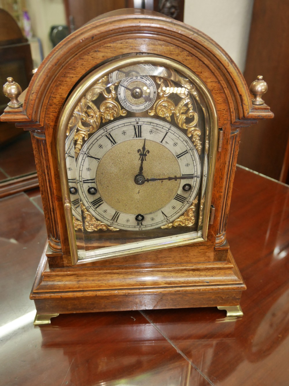 An antique arched walnut bracket clock with a brass-mounted silvered dial and corner finials.