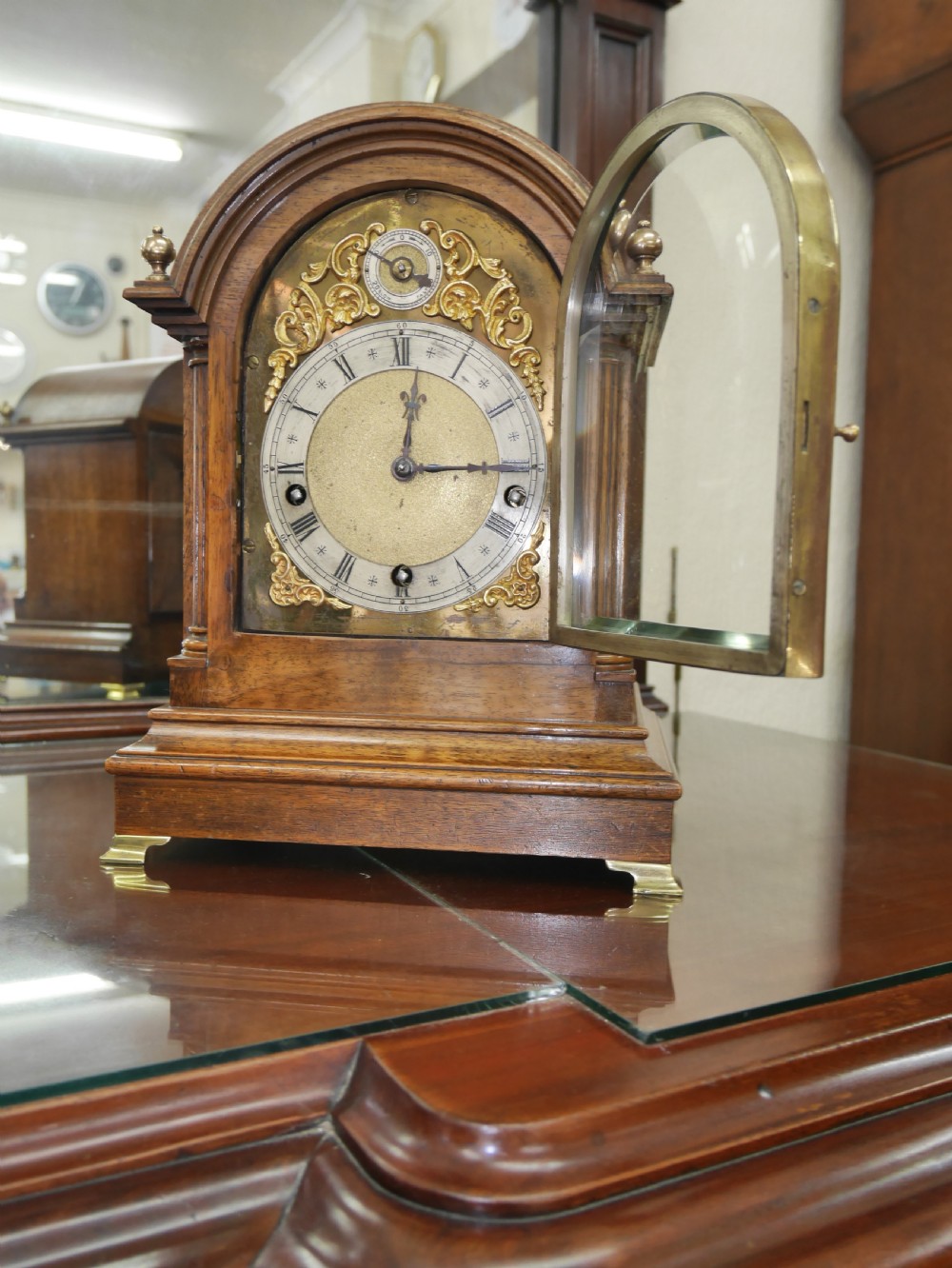 An antique arched walnut bracket clock with a brass-mounted silvered dial and corner finials. View II