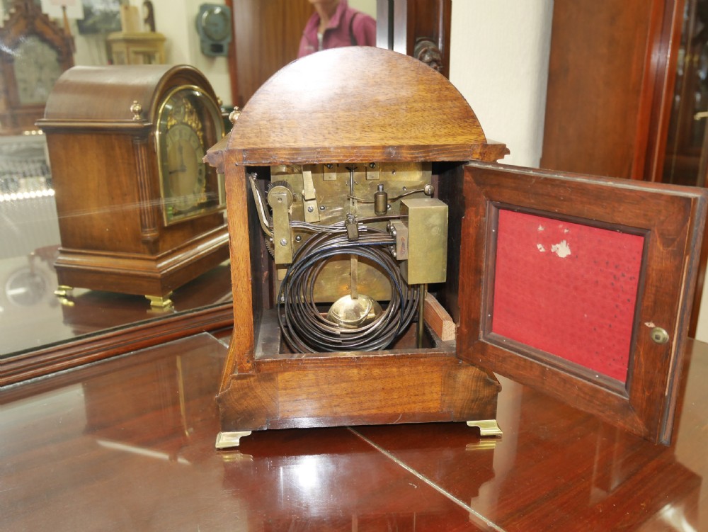 An antique arched walnut bracket clock with a brass-mounted silvered dial and corner finials. View IV