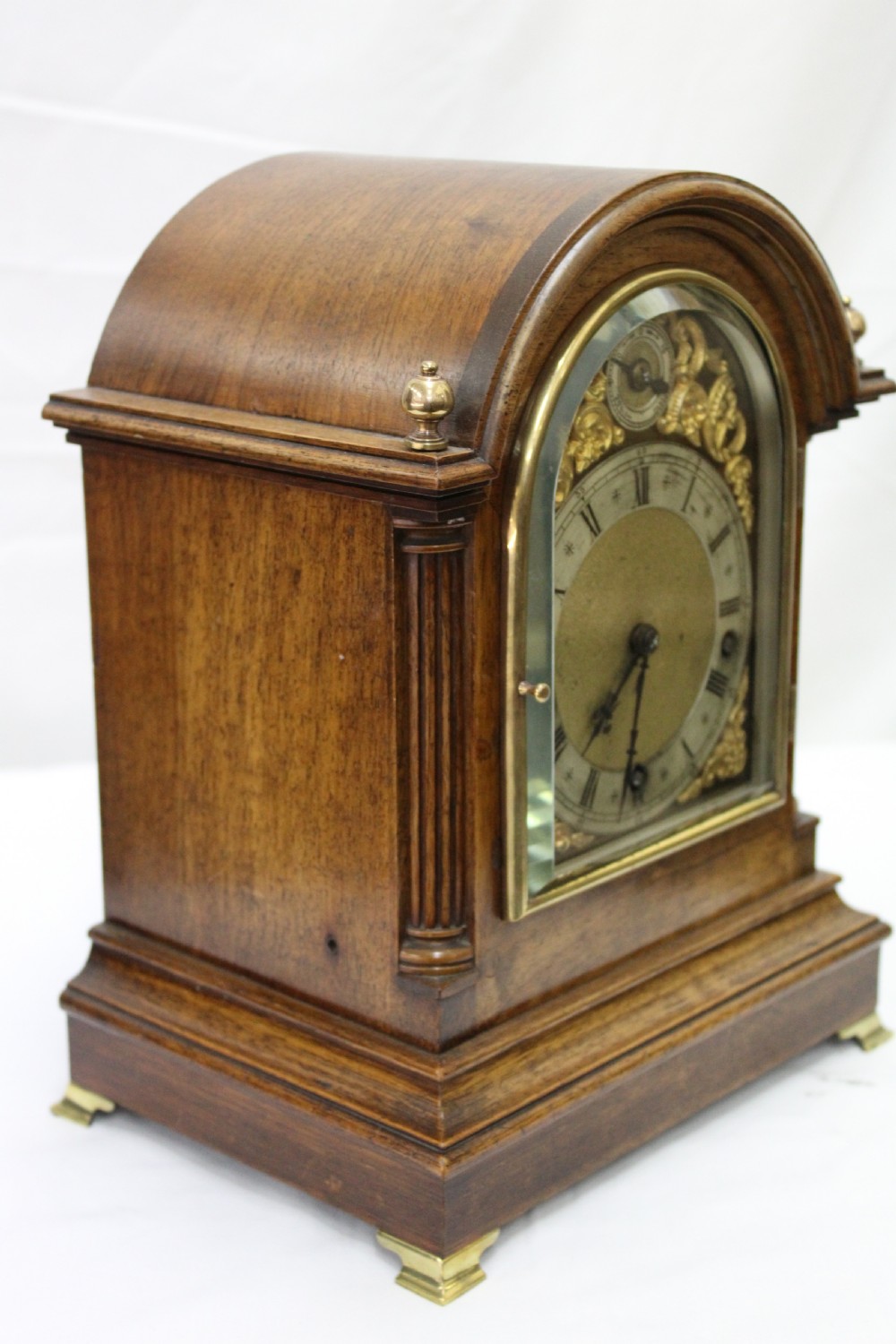 An antique arched walnut bracket clock with a brass-mounted silvered dial and corner finials. View V