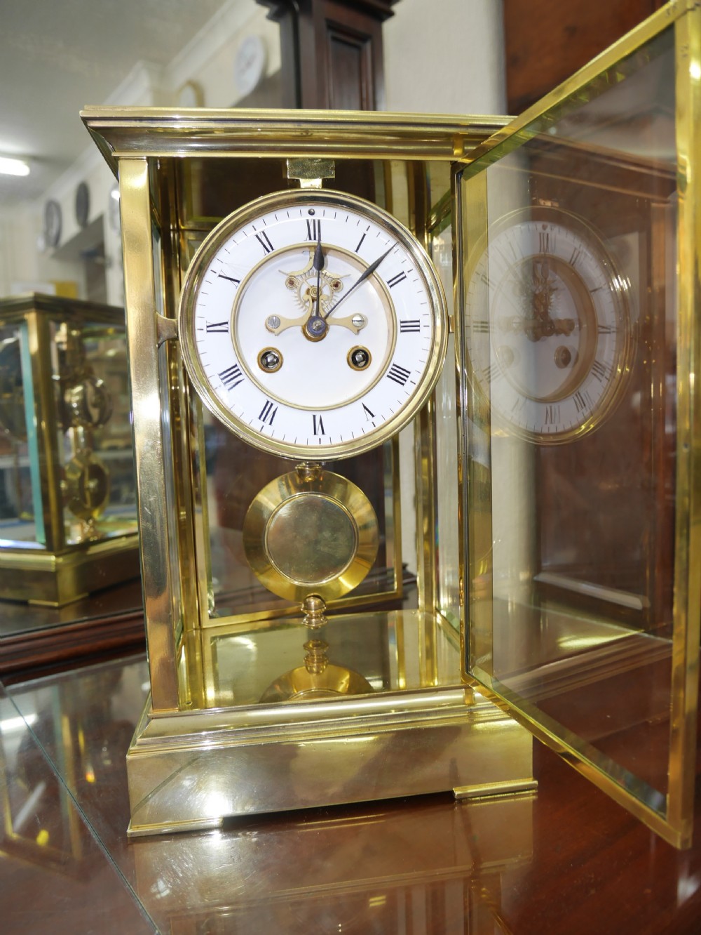 A late nineteenth-century brass four-glass mantel clock featuring a white enamel dial with Roman numerals and a visible brass pendulum. View II