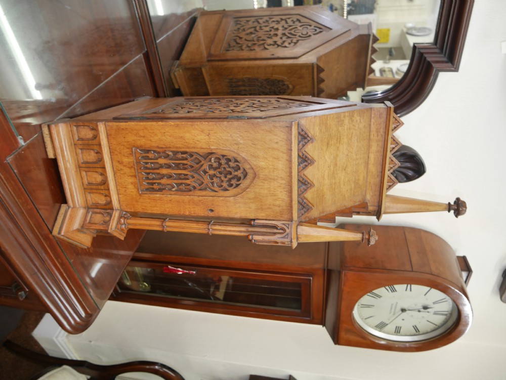 An English Gothic Revival wooden bracket clock featuring carved spires, pointed arches, traceried arcading, and an engraved metal dial signed by John Bennett. View II