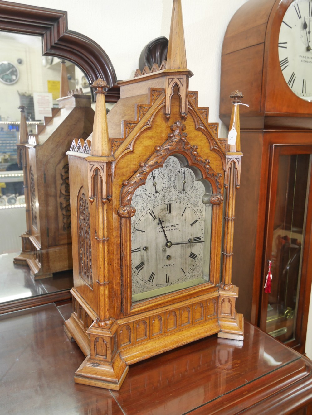 An English Gothic Revival wooden bracket clock featuring carved spires, pointed arches, traceried arcading, and an engraved metal dial signed by John Bennett. View IV