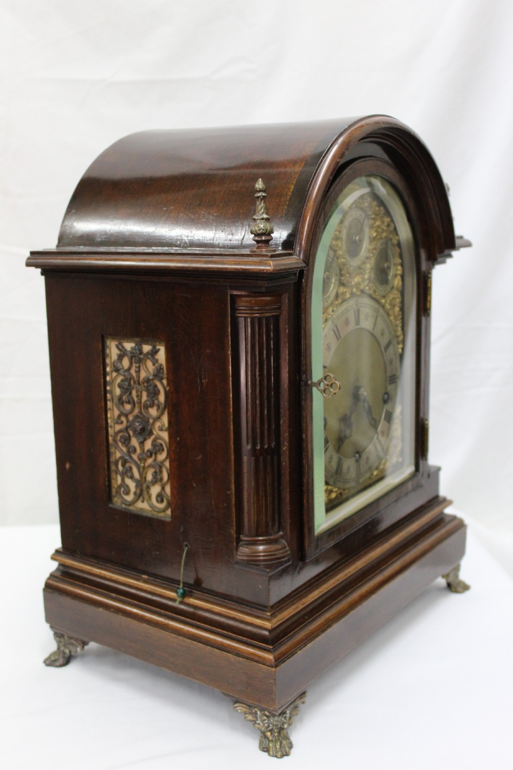 An arched mahogany bracket clock featuring brass spandrels, subsidiary dials, a silvered chapter ring, and brass bracket feet. View VIII