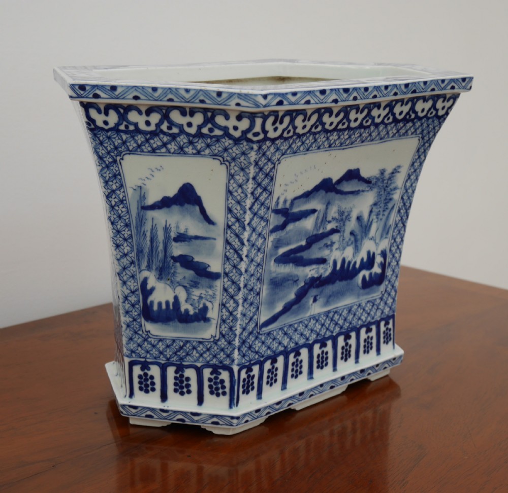 A rectangular blue and white ceramic jardiniere decorated with painted Chinese landscape panels and geometric lattice borders.