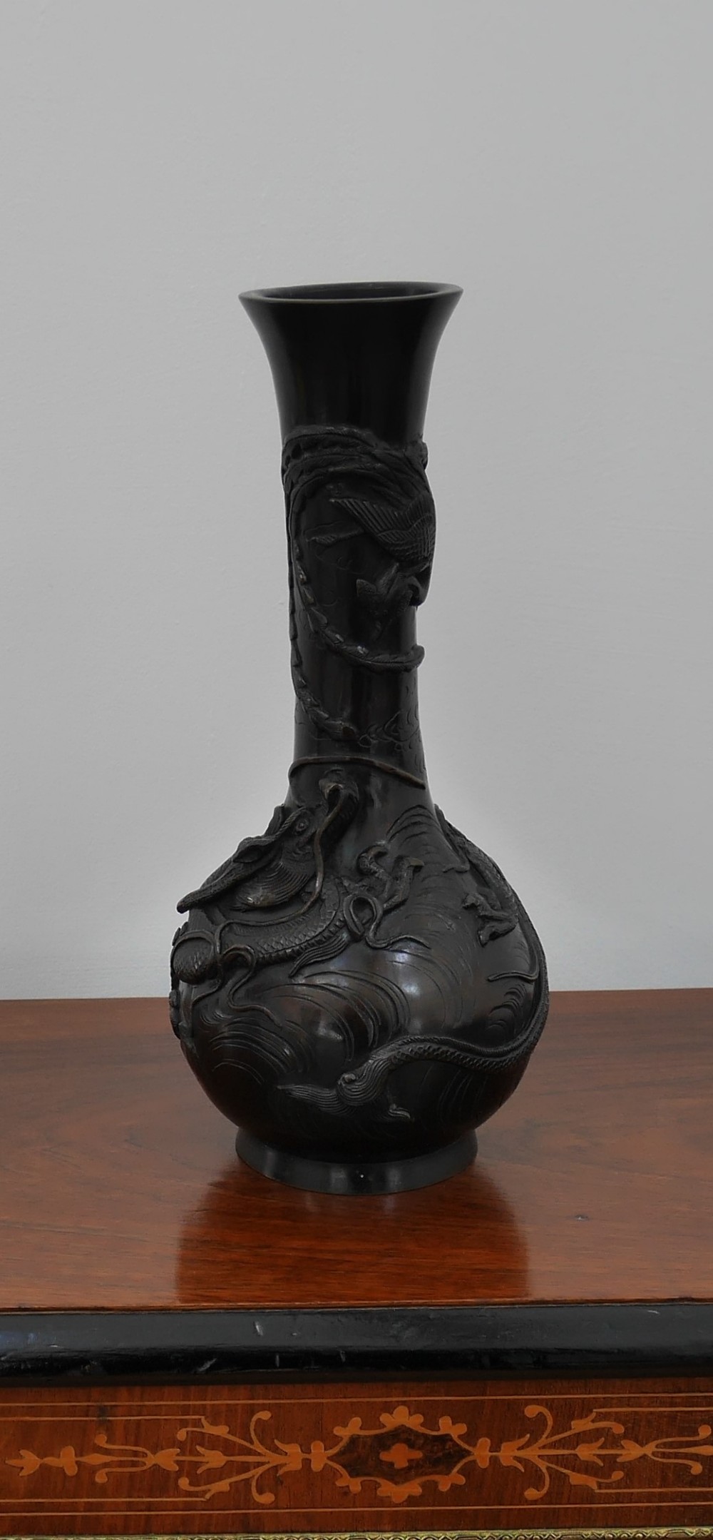 A dark brown patinated bronze vase featuring a flared neck and bulbous body decorated with high-relief dragon motifs.