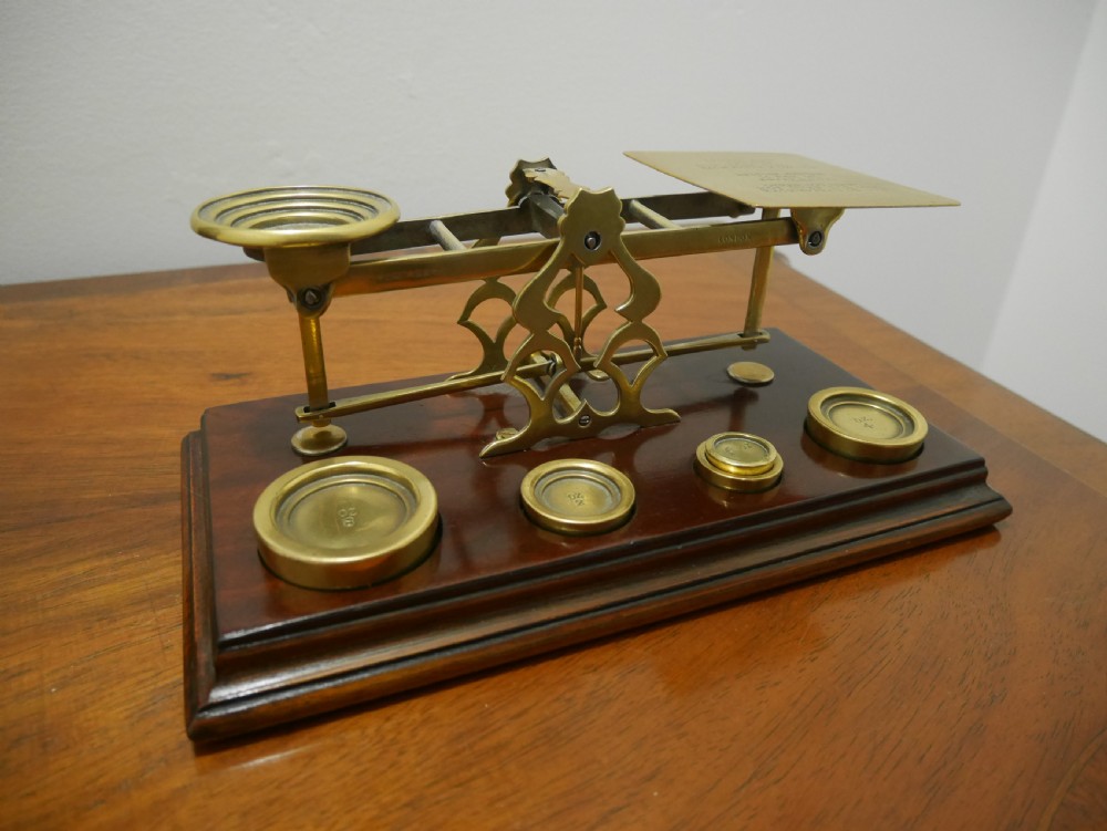 Victorian brass letter scales with engraved postal rates mounted on a dark mahogany base beside four nested brass weights. View II