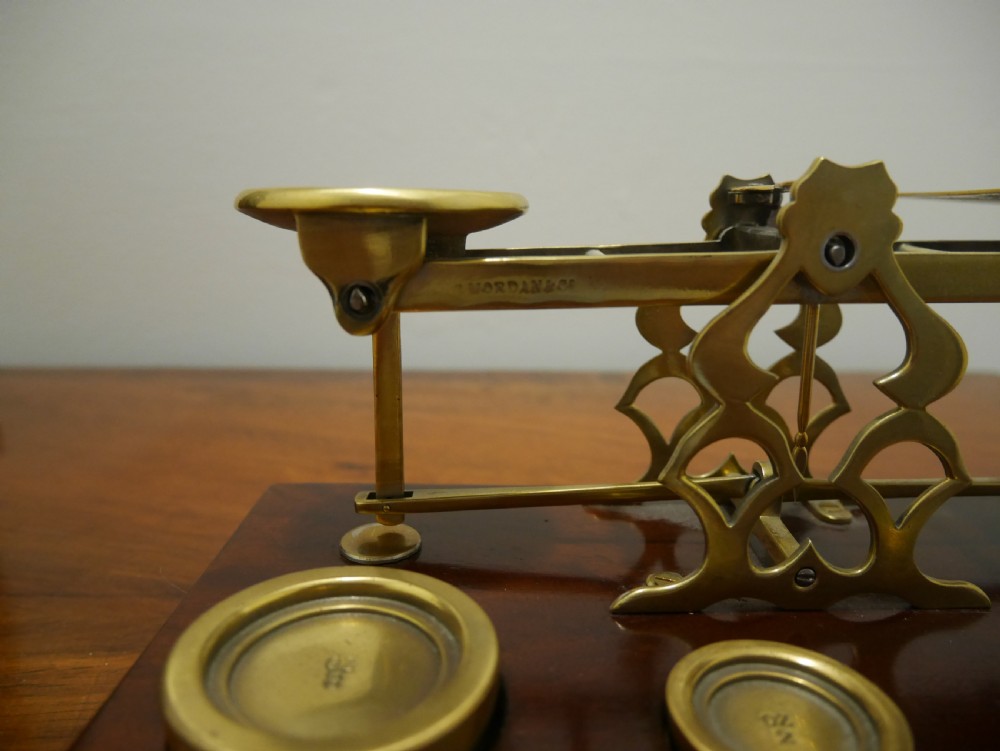 Victorian brass letter scales with engraved postal rates mounted on a dark mahogany base beside four nested brass weights. View III
