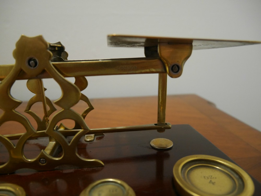 Victorian brass letter scales with engraved postal rates mounted on a dark mahogany base beside four nested brass weights. View IV