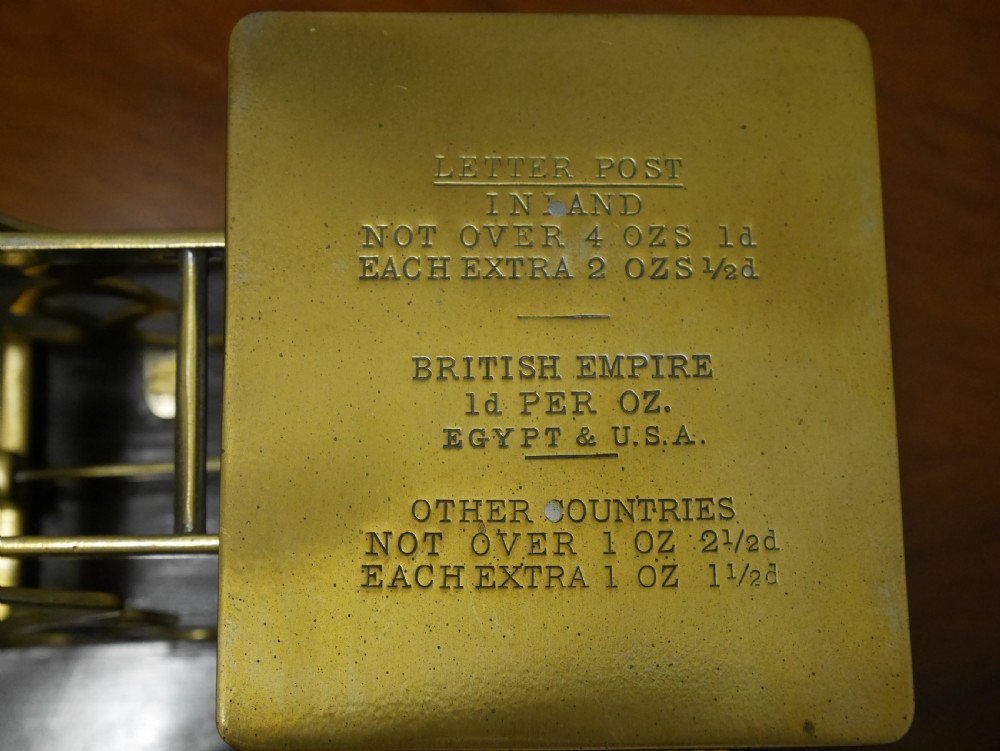 Victorian brass letter scales with engraved postal rates mounted on a dark mahogany base beside four nested brass weights. View V