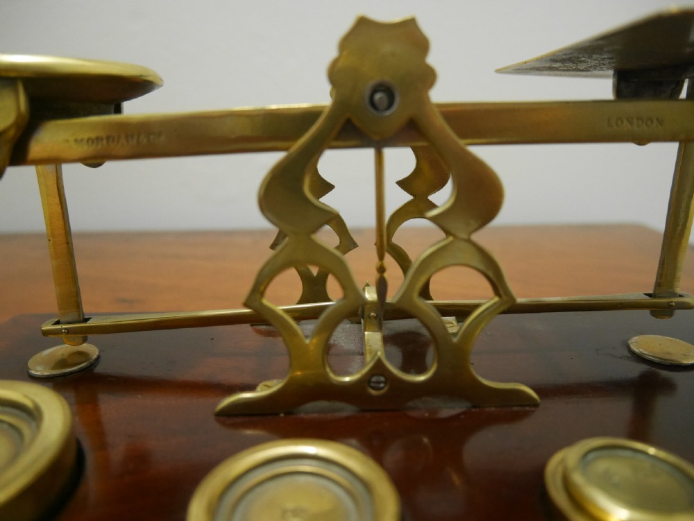 Victorian brass letter scales with engraved postal rates mounted on a dark mahogany base beside four nested brass weights. View VI