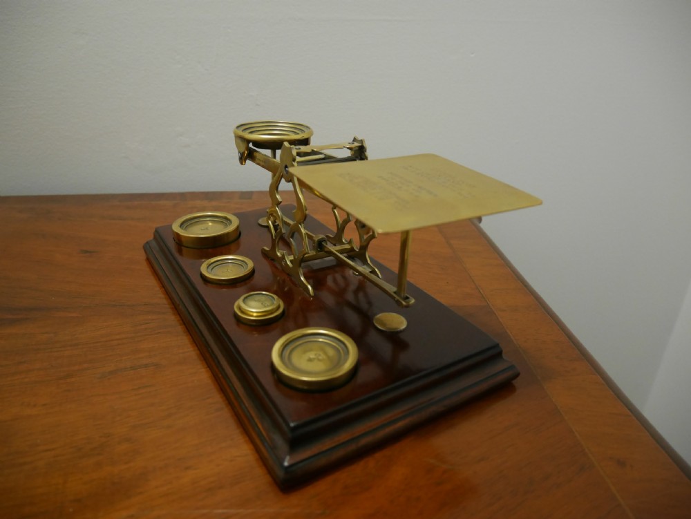 Victorian brass letter scales with engraved postal rates mounted on a dark mahogany base beside four nested brass weights. View VII
