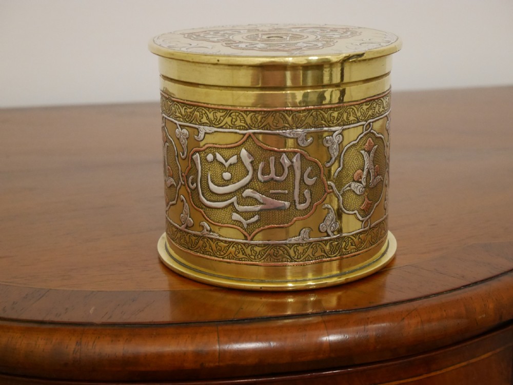 A cylindrical brass artillery shell casing converted into a lidded container with silver and copper Middle Eastern calligraphy inlays. View II