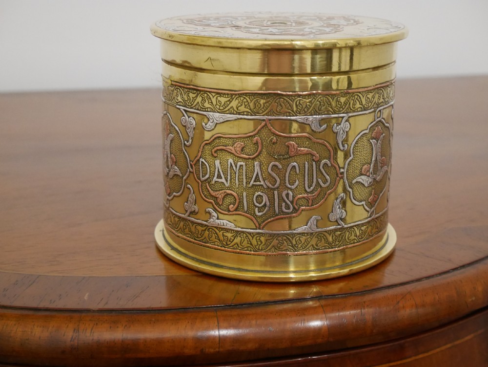 A cylindrical brass artillery shell casing converted into a lidded container with silver and copper Middle Eastern calligraphy inlays. View III