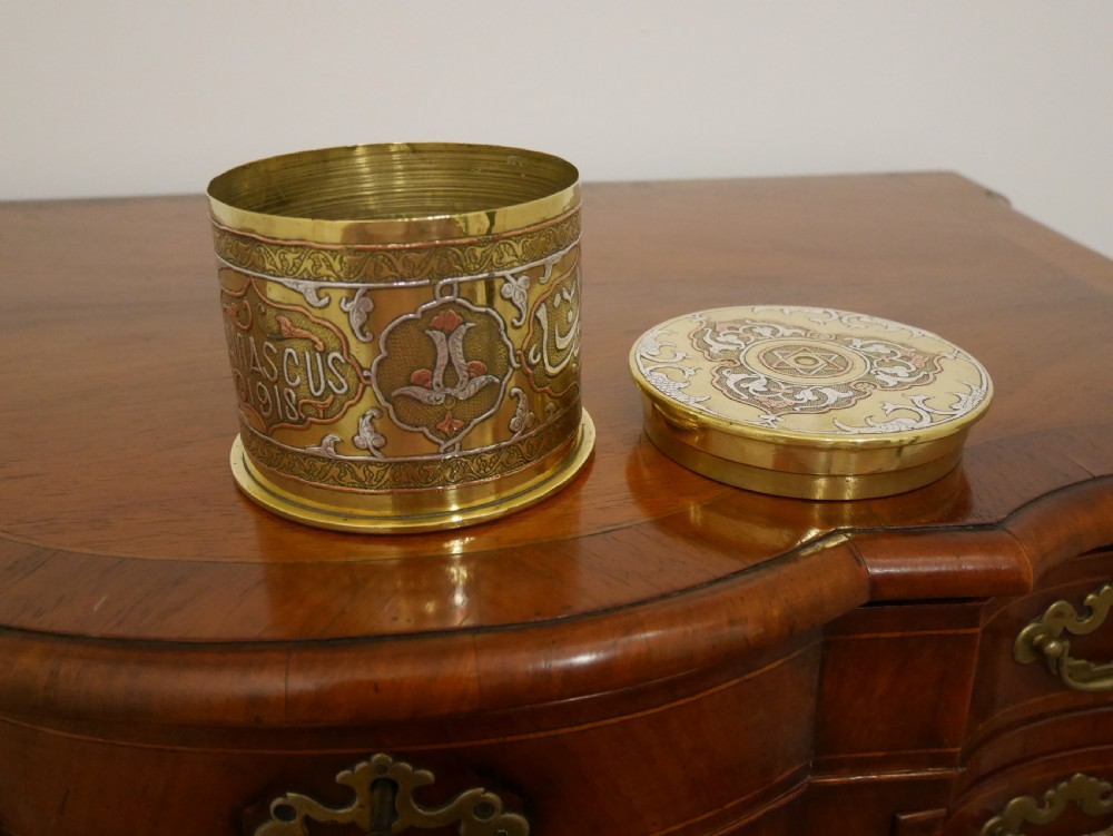 A cylindrical brass artillery shell casing converted into a lidded container with silver and copper Middle Eastern calligraphy inlays. View IV