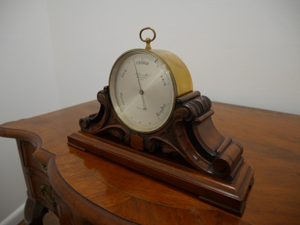 A mid-Victorian aneroid desk barometer mounted in a carved mahogany case on a stepped base with a brass dial bezel. View III