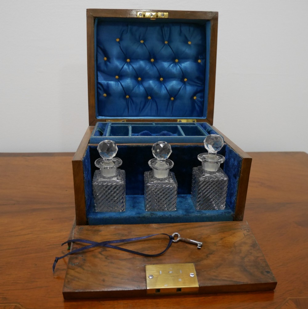 An open Victorian walnut dressing box featuring a blue button-tufted lining, three cut glass scent bottles, and brass hardware.