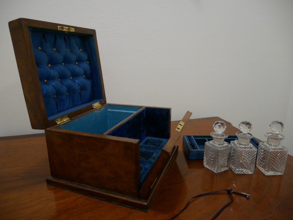 An open Victorian walnut dressing box featuring a blue button-tufted lining, three cut glass scent bottles, and brass hardware. View III