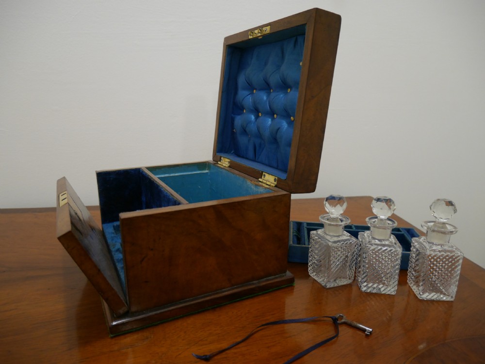 An open Victorian walnut dressing box featuring a blue button-tufted lining, three cut glass scent bottles, and brass hardware. View IV