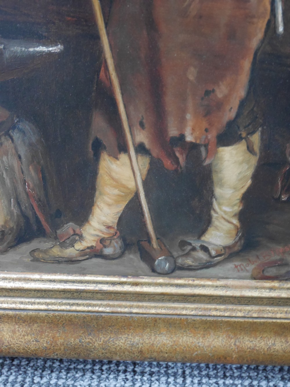 A framed oil painting depicting a blacksmith standing in profile inside a forge, holding a sledgehammer while wearing an apron, presented in a wide gilded frame. View II