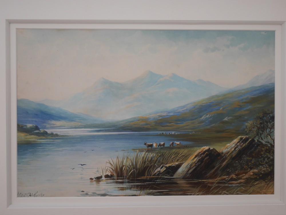A framed gouache landscape painting depicting a mountain lake scene with cattle near the water edge, set in a light timber frame. View II