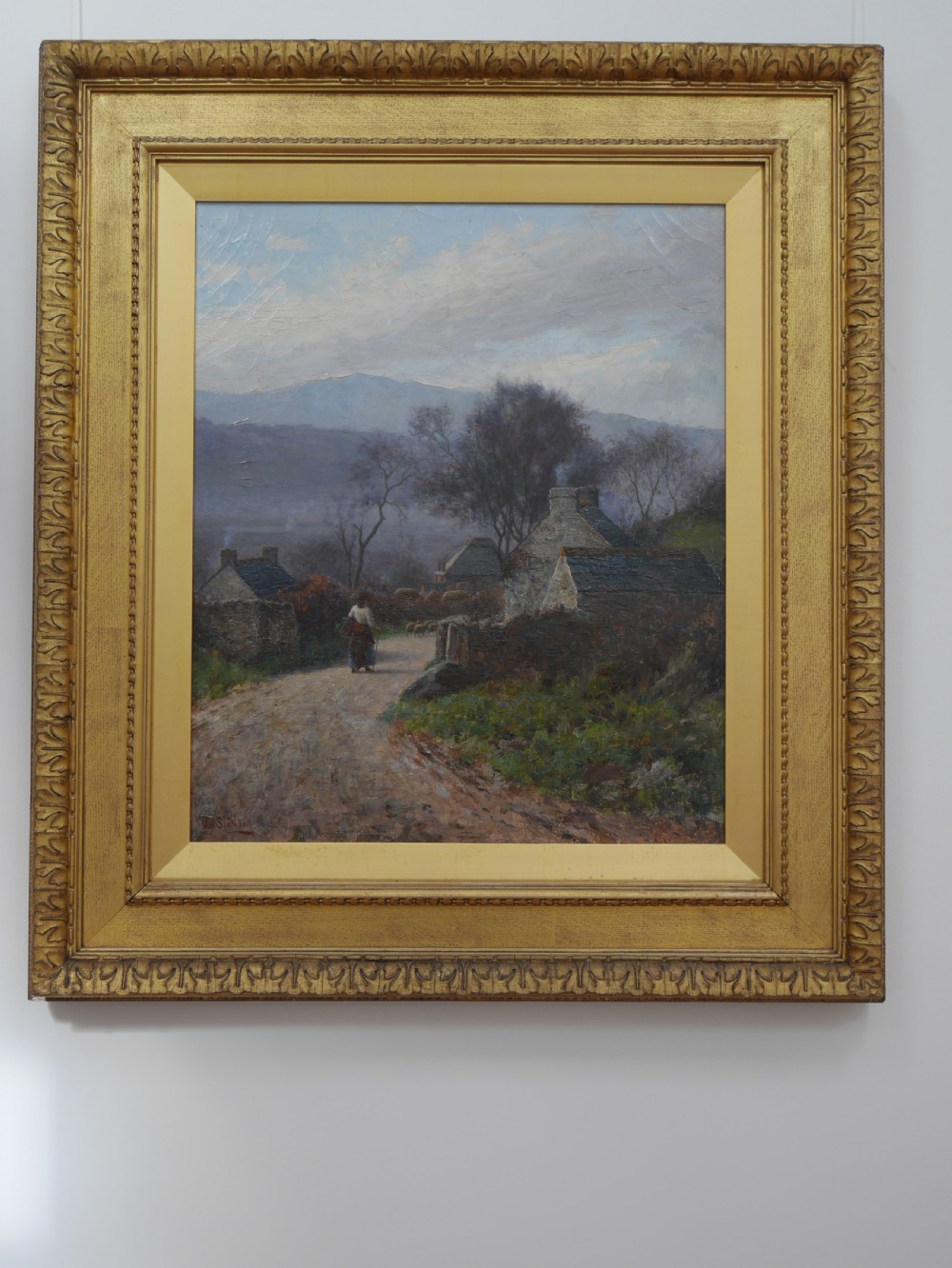 An antique oil painting on canvas depicting a rural stone cottage along a dirt path set in an ornate carved giltwood frame.
