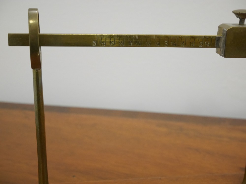 An antique brass balance scale featuring a graduated measurement beam, sliding weight, and single suspended pan mounted on a mahogany base. View II