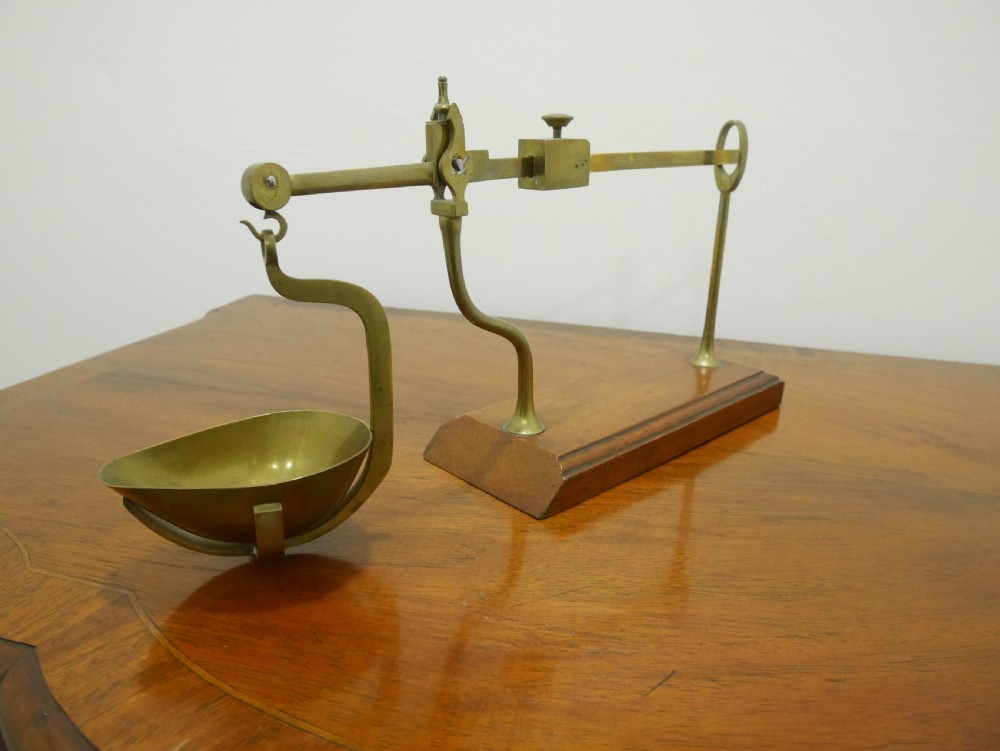 An antique brass balance scale featuring a graduated measurement beam, sliding weight, and single suspended pan mounted on a mahogany base. View V