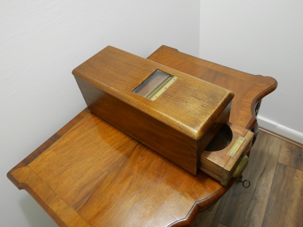 An open mahogany Gledhill patent cash till showing internal mechanical brass parts, a paper roll mechanism, and a printed paper instruction label on the underside of the lid. View II