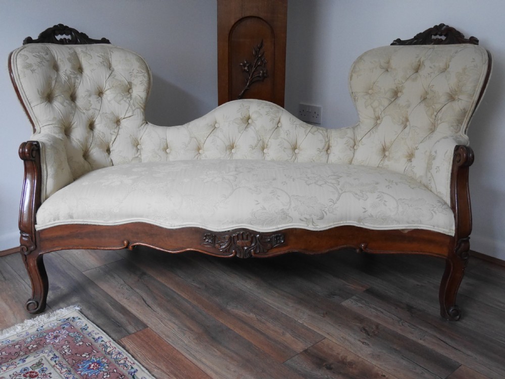 A Victorian double end settee with a carved mahogany frame, cabriole legs, and button-tufted cream damask upholstery.