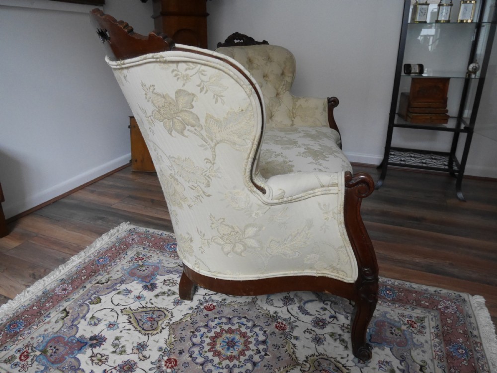 A Victorian double end settee with a carved mahogany frame, cabriole legs, and button-tufted cream damask upholstery. View II