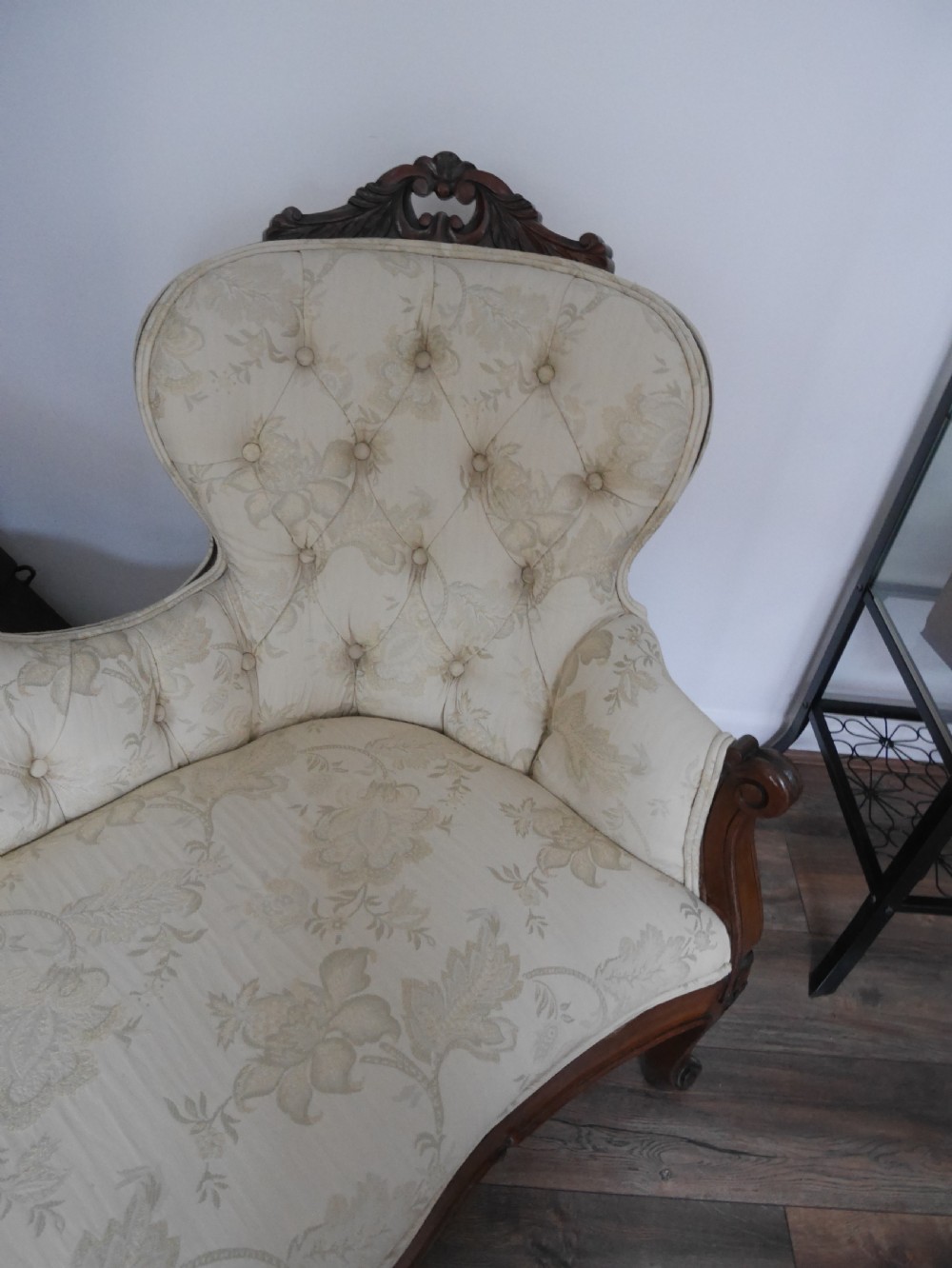 A Victorian double end settee with a carved mahogany frame, cabriole legs, and button-tufted cream damask upholstery. View IV