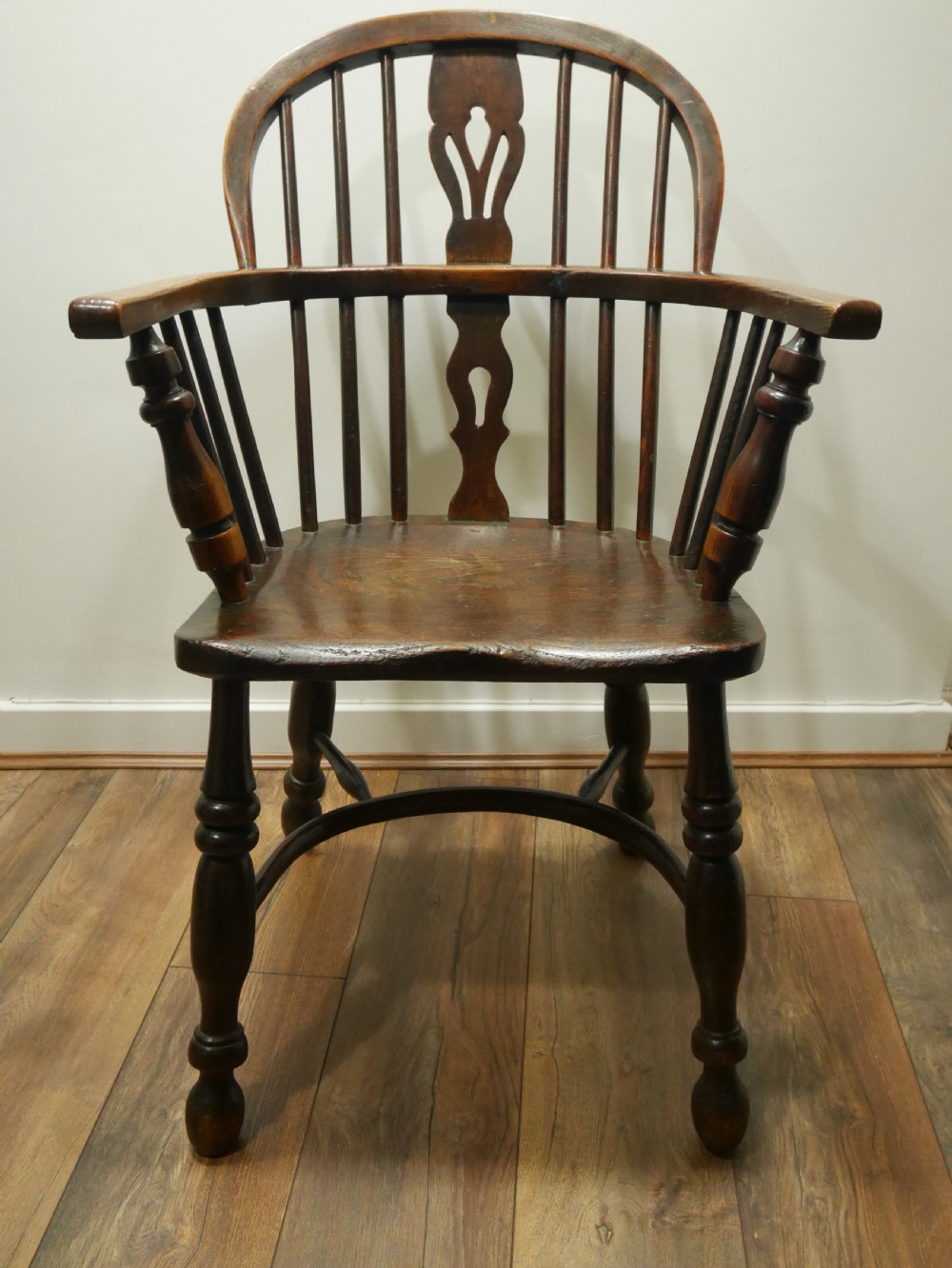 A dark brown antique wooden Windsor armchair featuring a hoop back with a central pierced splat, spindled backrest, shaped seat, turned legs, and a stretcher base.