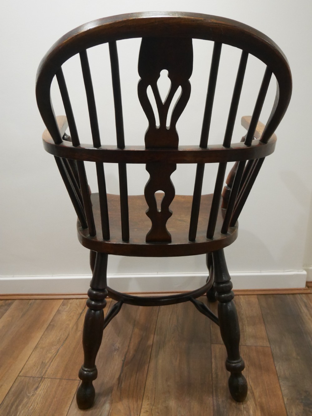 A dark brown antique wooden Windsor armchair featuring a hoop back with a central pierced splat, spindled backrest, shaped seat, turned legs, and a stretcher base. View III