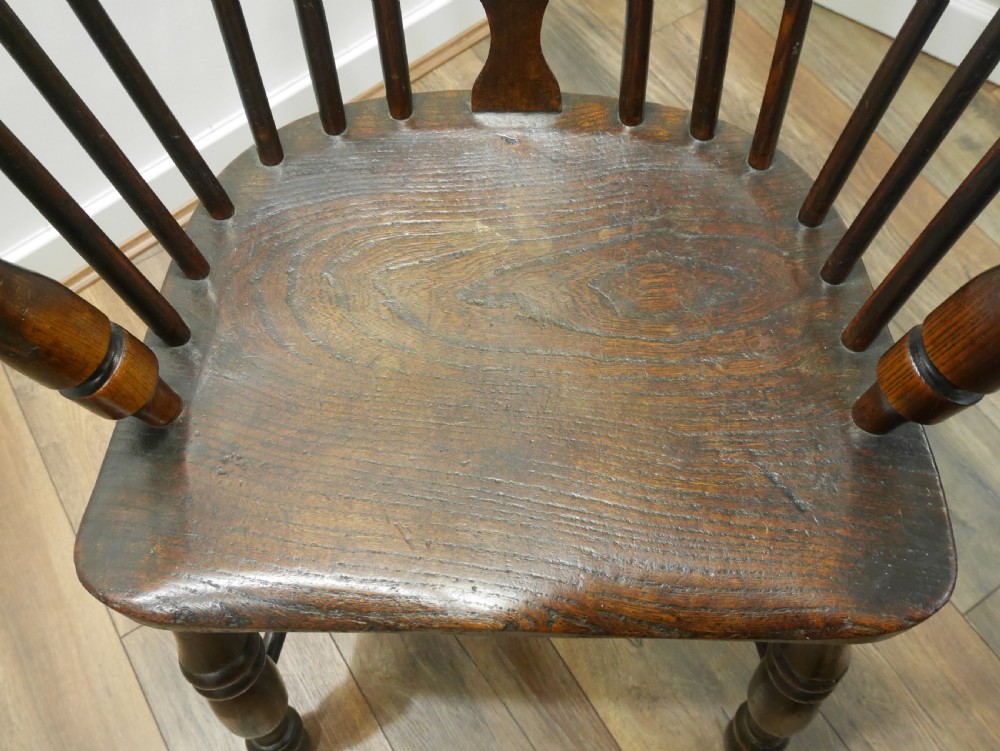 A dark brown antique wooden Windsor armchair featuring a hoop back with a central pierced splat, spindled backrest, shaped seat, turned legs, and a stretcher base. View V