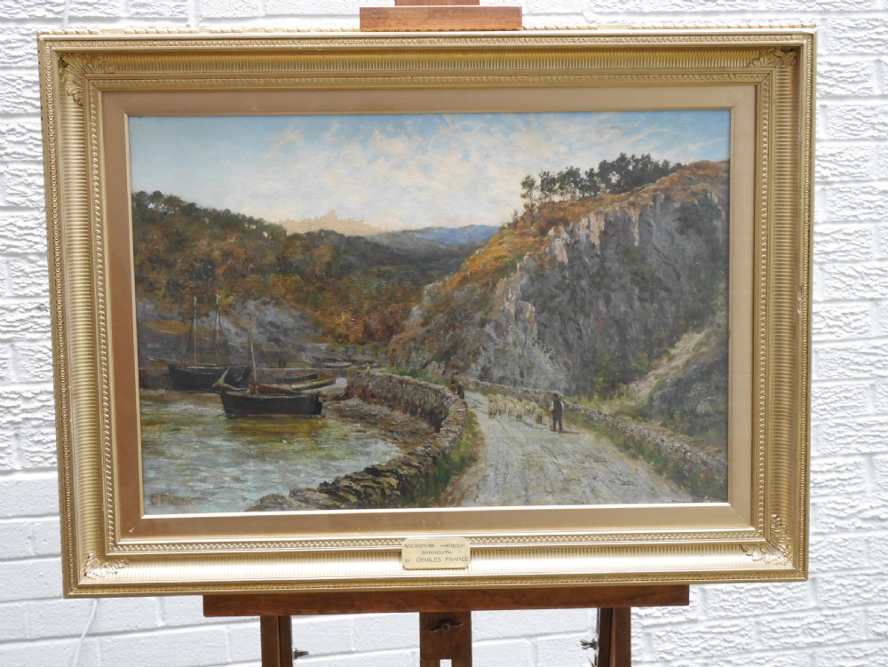 An oil painting on canvas depicting Aberamffra Harbour with moored boats and a shepherd on a stone road, set in a gilded frame.
