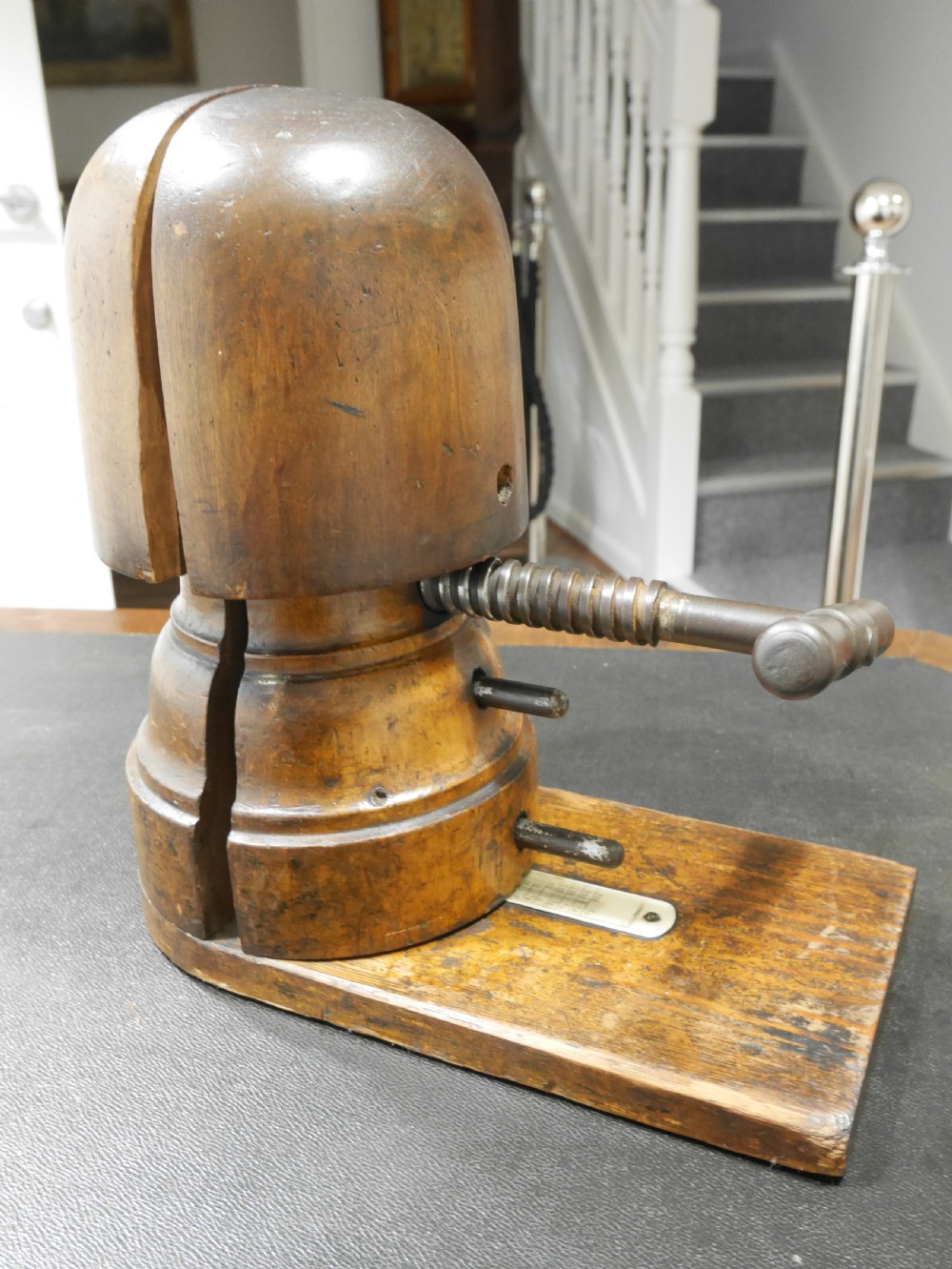 An antique wooden hat stretcher featuring a split crown block mounted on a flat wooden base with a metal threaded screw handle mechanism. View II