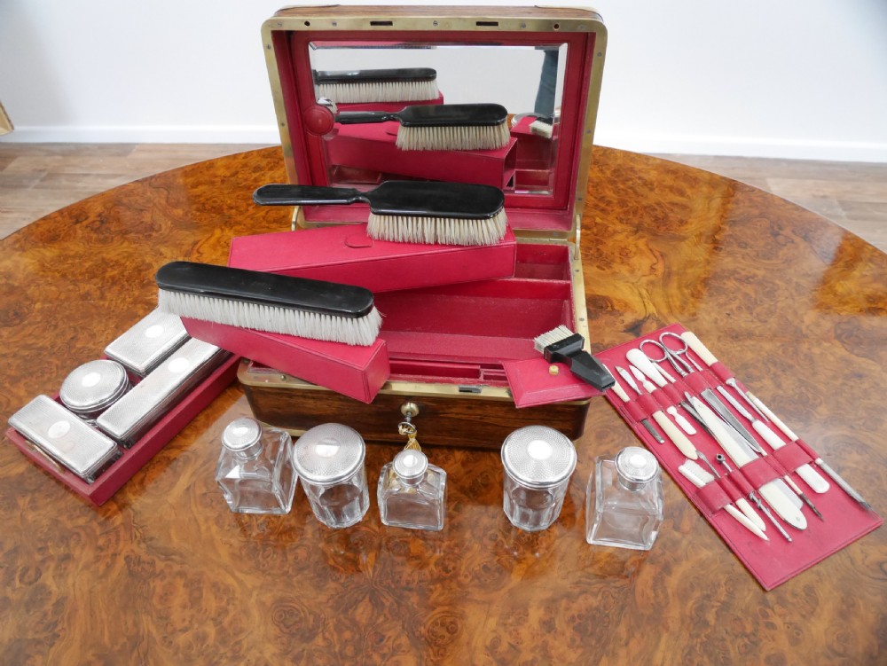 An open antique brass-bound wooden dressing box featuring a red velvet interior, integrated lid mirror, and fitted glass bottles with metal caps. View III