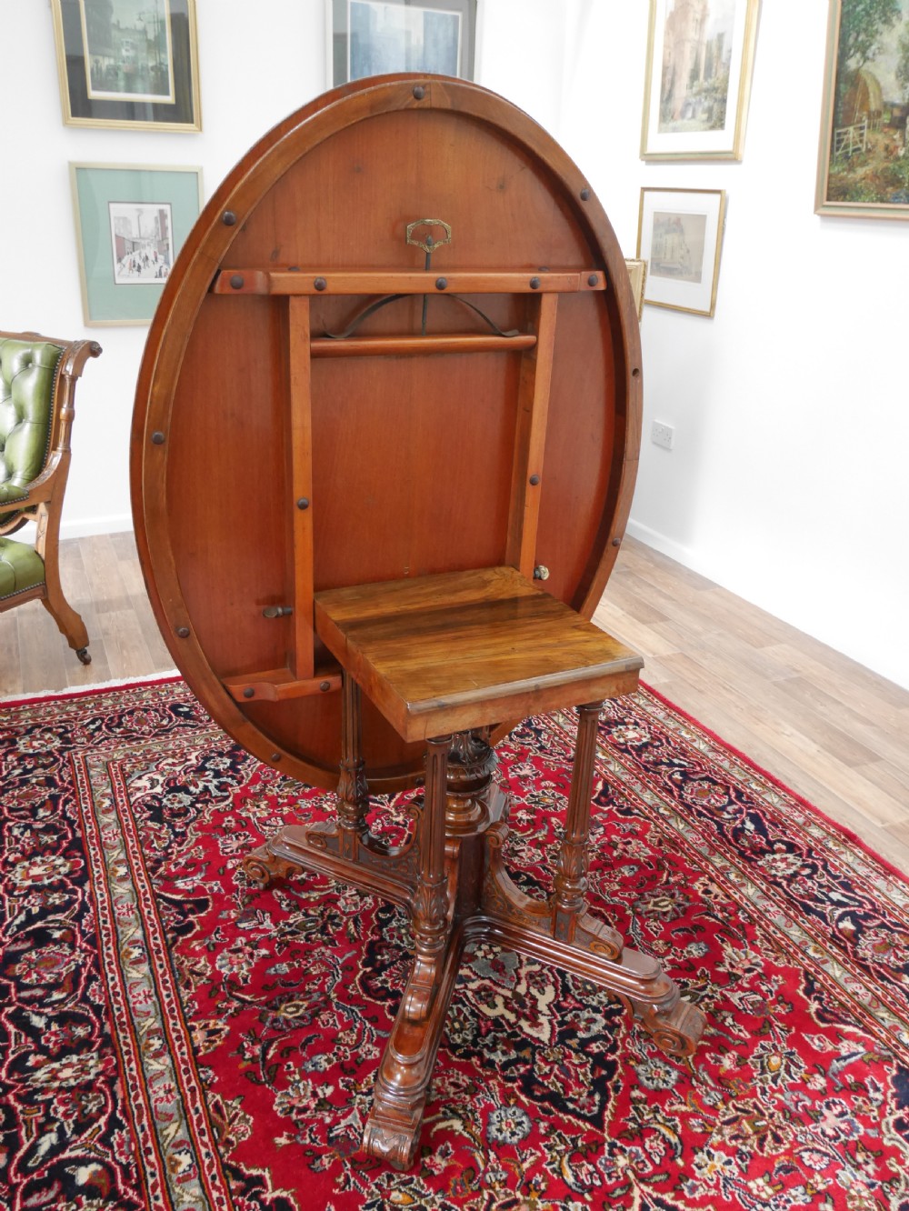 An oval Victorian burr walnut tilt-top loo table featuring figured timber grain and a carved central pedestal base with four scroll feet. View III