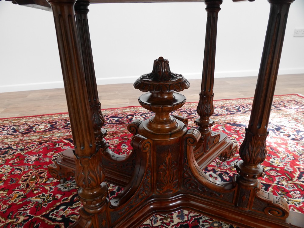 An oval Victorian burr walnut tilt-top loo table featuring figured timber grain and a carved central pedestal base with four scroll feet. View VI