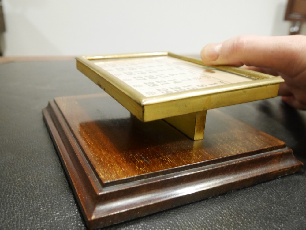 A vintage perpetual desk calendar with a polished brass frame holding paper month cards, mounted on a dark mahogany wooden base. View V