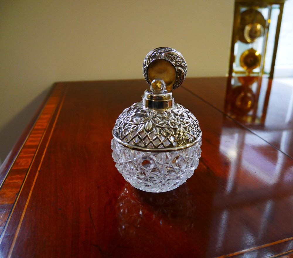 A globular cut glass scent bottle featuring an embossed silver mount with floral lattice detailing and a silver cap. View II