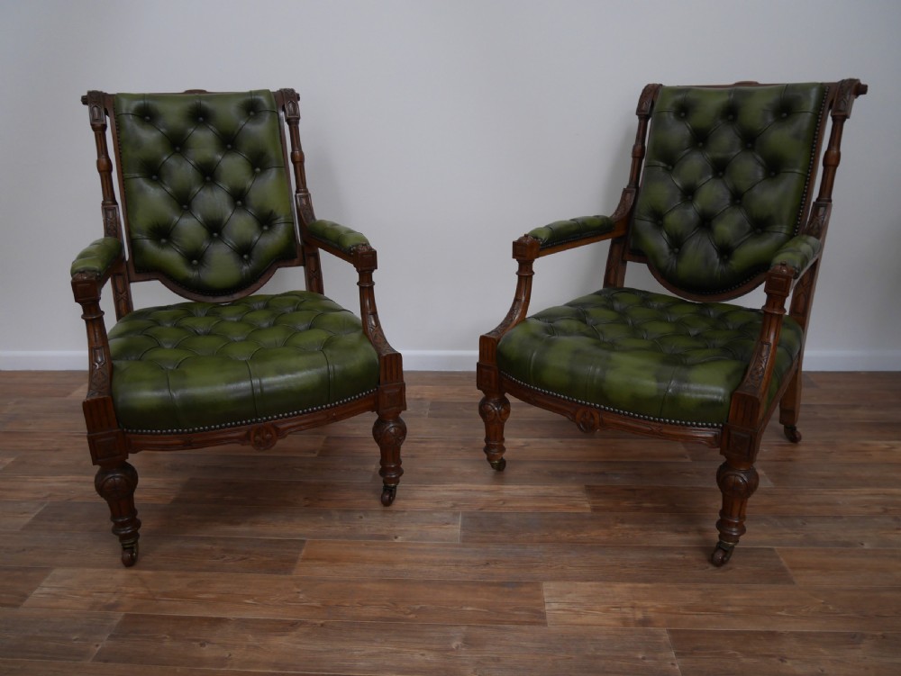 A pair of Victorian mahogany armchairs upholstered in deep-buttoned olive green leather with carved frames and brass castors.