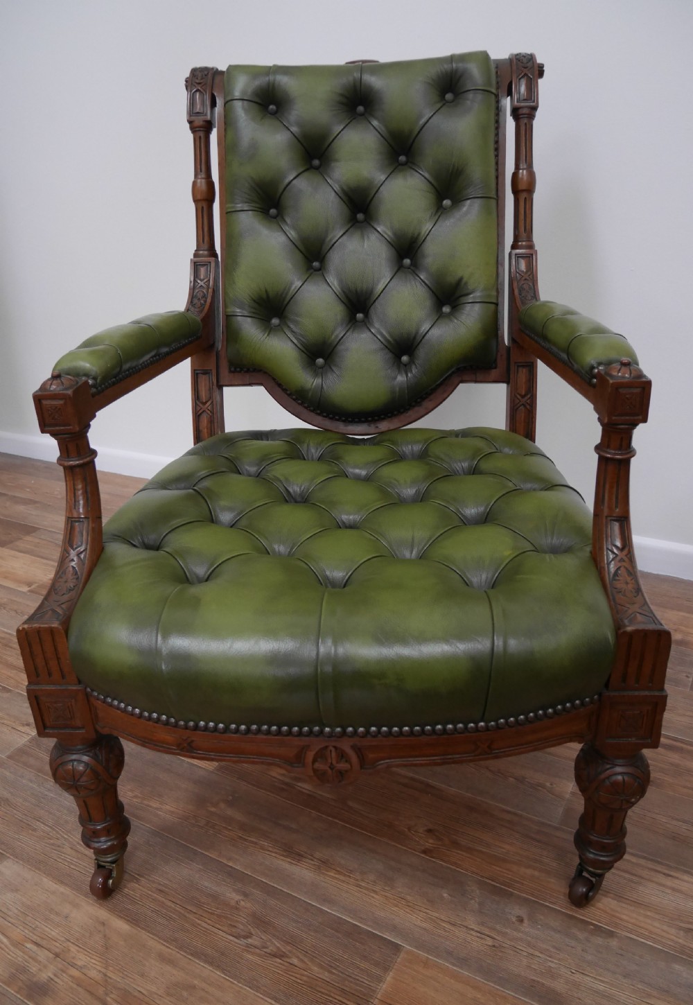 A pair of Victorian mahogany armchairs upholstered in deep-buttoned olive green leather with carved frames and brass castors. View II