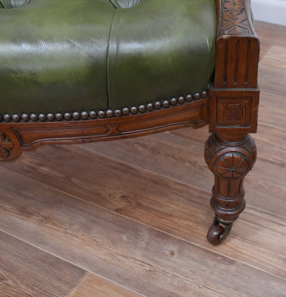 A pair of Victorian mahogany armchairs upholstered in deep-buttoned olive green leather with carved frames and brass castors. View III