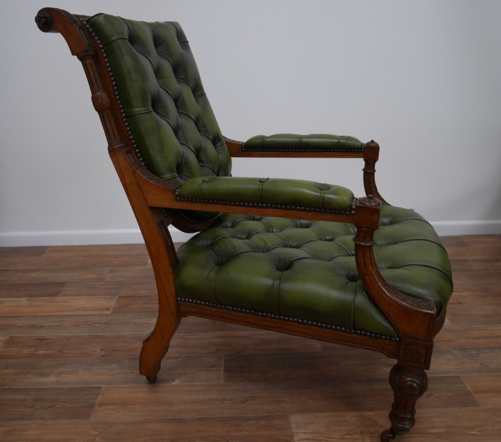 A pair of Victorian mahogany armchairs upholstered in deep-buttoned olive green leather with carved frames and brass castors. View V