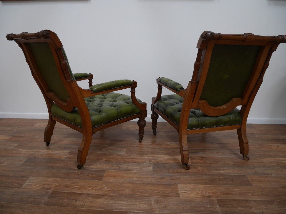 A pair of Victorian mahogany armchairs upholstered in deep-buttoned olive green leather with carved frames and brass castors. View VI