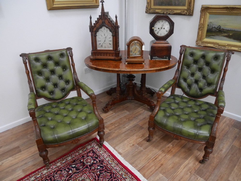 A pair of Victorian mahogany armchairs upholstered in deep-buttoned olive green leather with carved frames and brass castors. View VIII