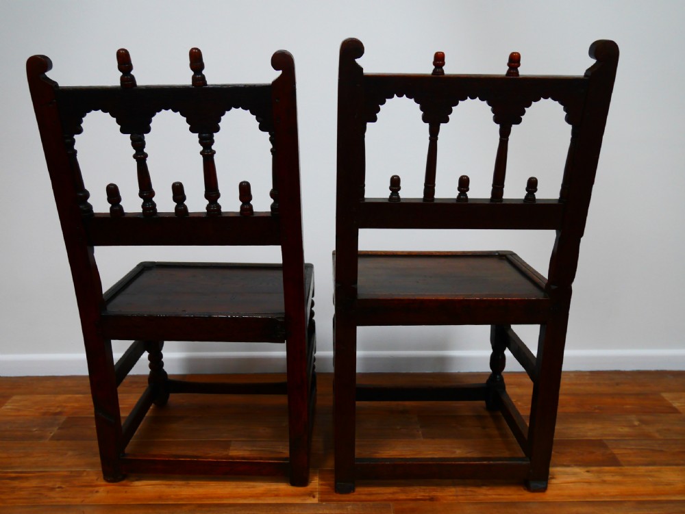 Pair of 17th-century dark oak Derbyshire side chairs featuring arcaded back rails with turned finials and solid wood panel seats. View V